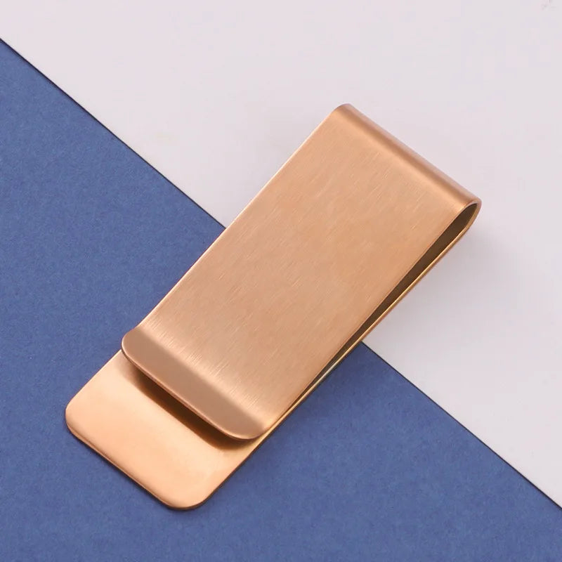 A rectangular rose gold metal tie clip lying on a blue-gray surface.
