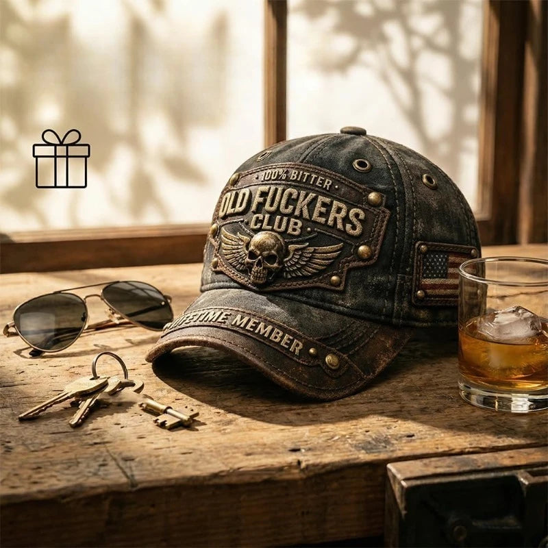 Mørk baseballcap med brodert tekst og skinnbundet gaveeske på treflate.