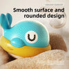 A blue and yellow musical light-up whale baby bath toy with a smooth, rounded design resting on a soft, brown surface.