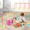 A child is building a colorful frame structure using straw building blocks on a wooden floor.