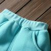 Close-up of a light blue fleece pajama set with ribbed cuffs and a pocket on a wooden surface.