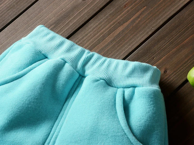 Close-up of a light blue fleece pajama set with ribbed cuffs and a pocket on a wooden surface.