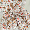 A white and floral cow print baby romper with a matching headband.
