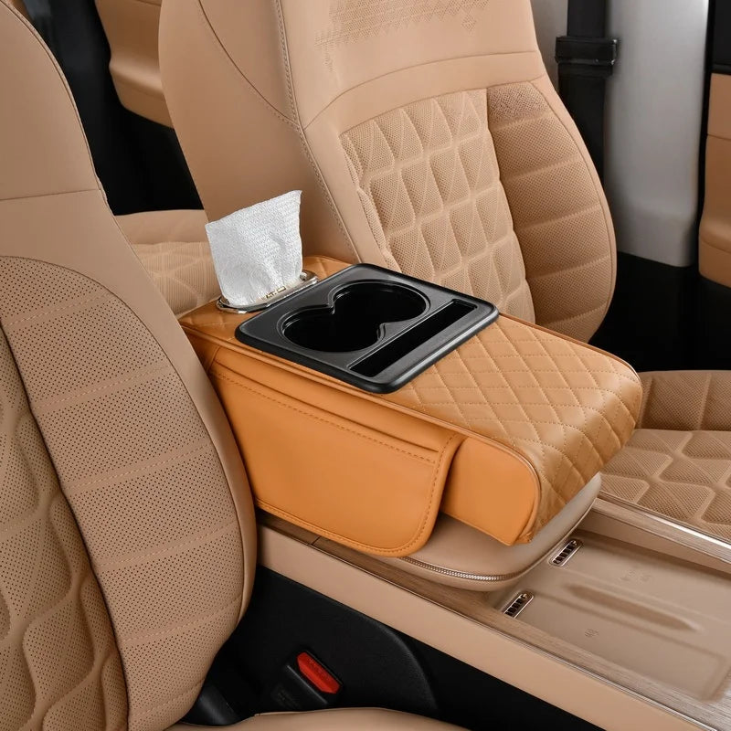 A tan car armrest cushion with a black dual cup holder is shown inside a vehicle interior.