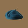 A dark teal wool beret hat resting on a plain brown background.