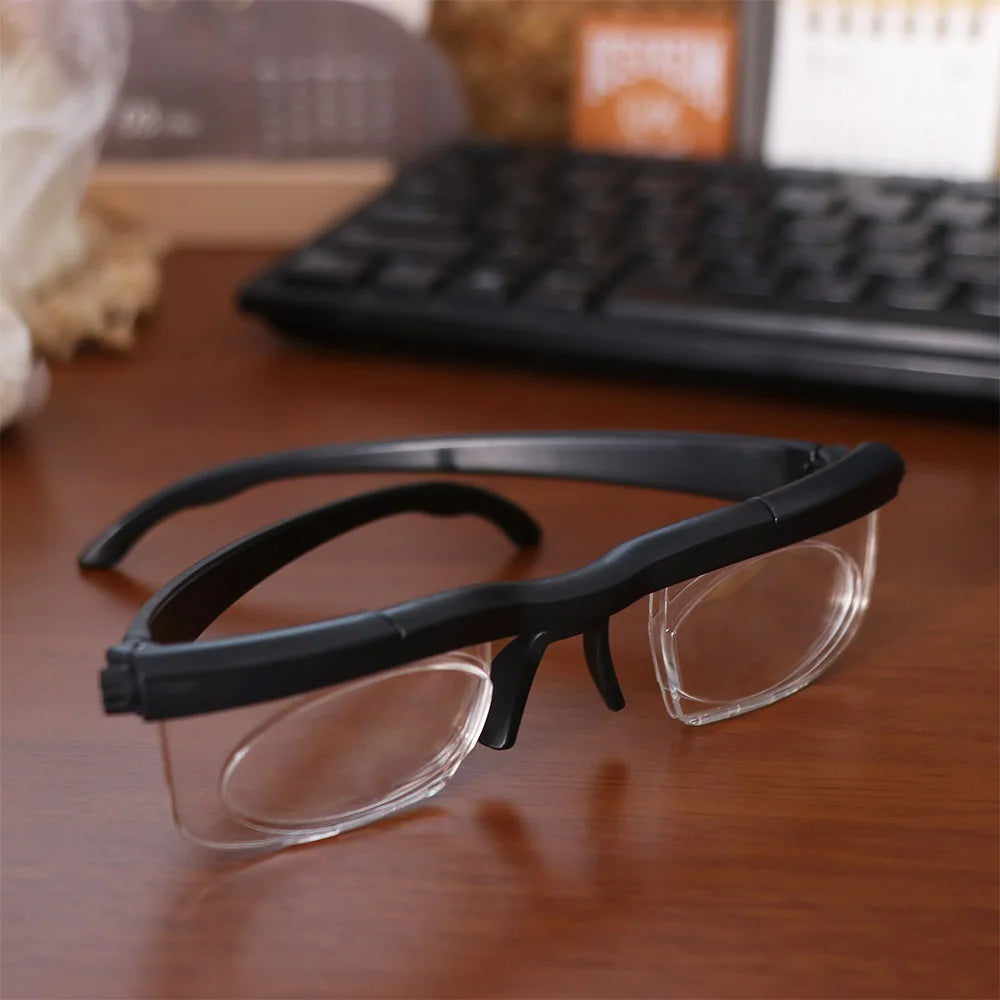 A pair of black adjustable focus reading and distance glasses resting on a wooden surface.