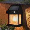 A black solar-powered motion sensor wall light with a glowing bulb mounted on an outdoor textured wall.
