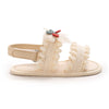 A pair of light beige baby girls' summer sandals with a bow embellishment and fluffy white trim.