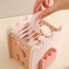A hand is placing a pink wooden mushroom castle stacking puzzle into its wooden frame.
