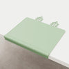 A light green silicone feeding placemat with a decorative teething edge resting on a light-colored surface.
