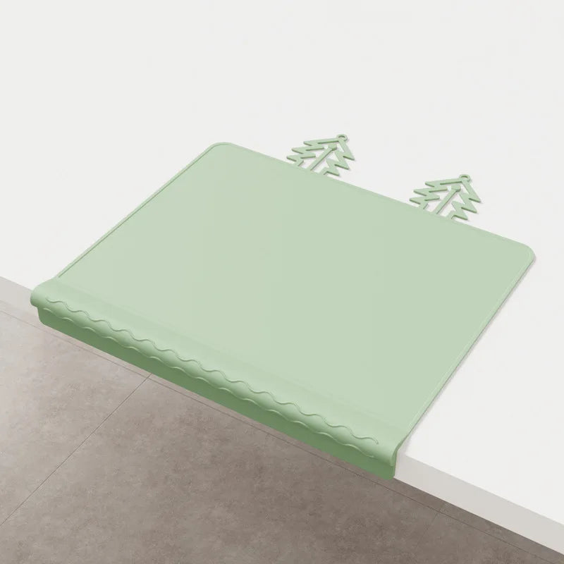 A light green silicone feeding placemat with a decorative teething edge resting on a light-colored surface.