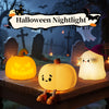 A glowing yellow silicone pumpkin night light sits on a wooden surface in a Halloween themed outdoor setting.