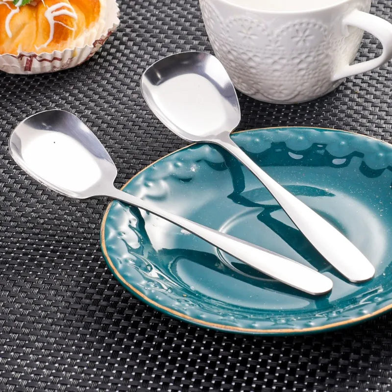 A stainless steel serving spoon rests on a teal plate on a dark textured surface next to a white cup.