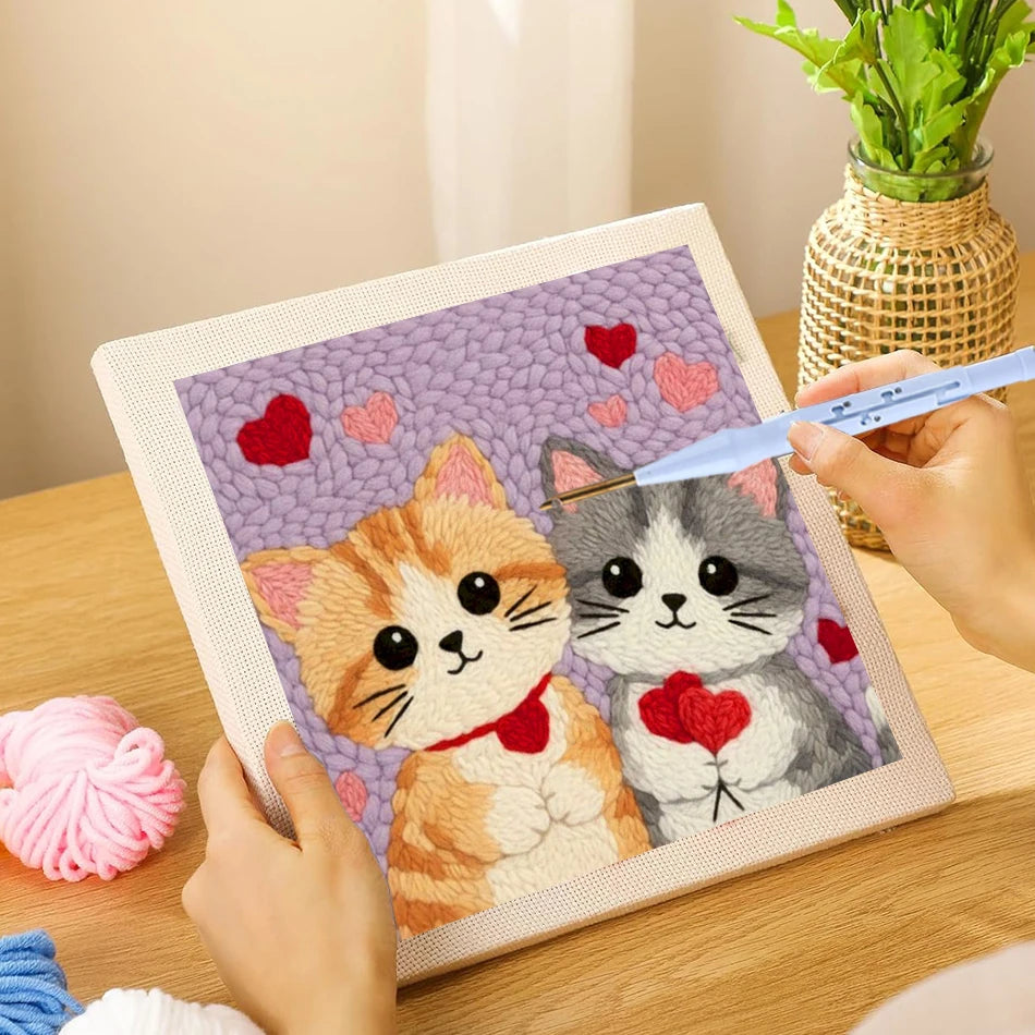 Una mano borda un diseño de gato y conejo en un lienzo cuadrado con hilos morados y rosas.