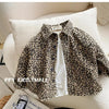 A beige leopard print denim jacket is displayed folded on a white cushion.