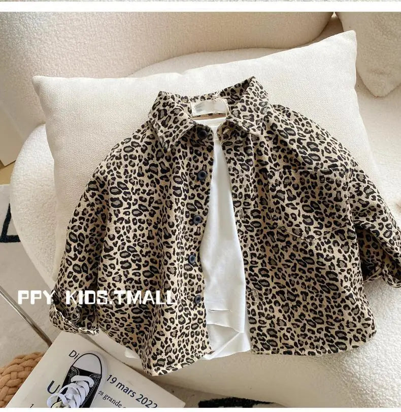 A beige leopard print denim jacket is displayed folded on a white cushion.
