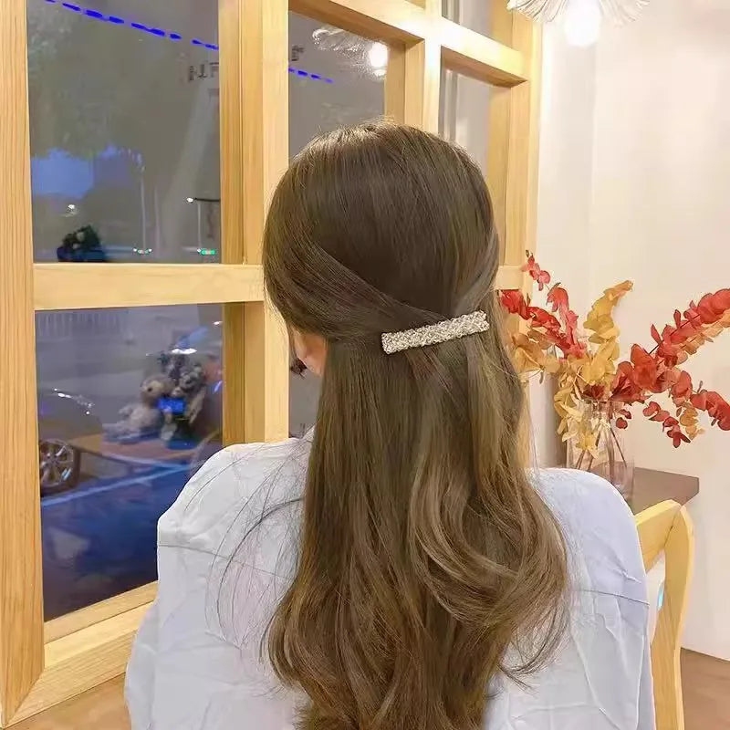 Mujer de pelo largo castaño vista desde atrás, con un clip de pelo de cristal y pedrería.