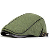A olive green knit newsboy cap with a dark trim and adjustable side buckle.