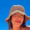 A woman wearing a woven straw crochet fisherman hat with a wide brim against a bright blue sky.