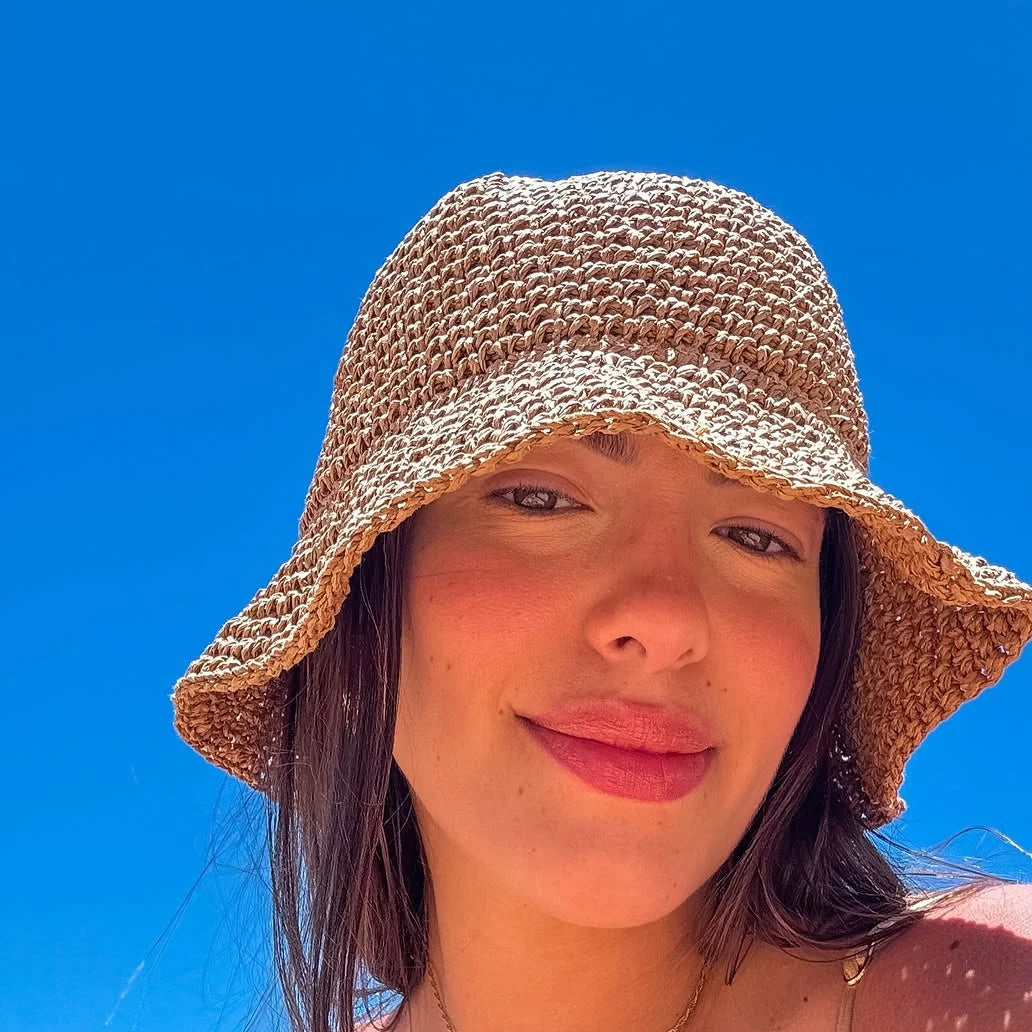 A woman wearing a woven straw crochet fisherman hat with a wide brim against a bright blue sky.