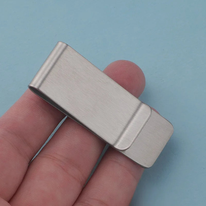 A close-up of a silver metal tie clip being held by a hand against a light blue background.