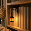 A vintage library lantern shelf lamp with a black metal stand and warm LED glow illuminates a row of light-colored cylindrica