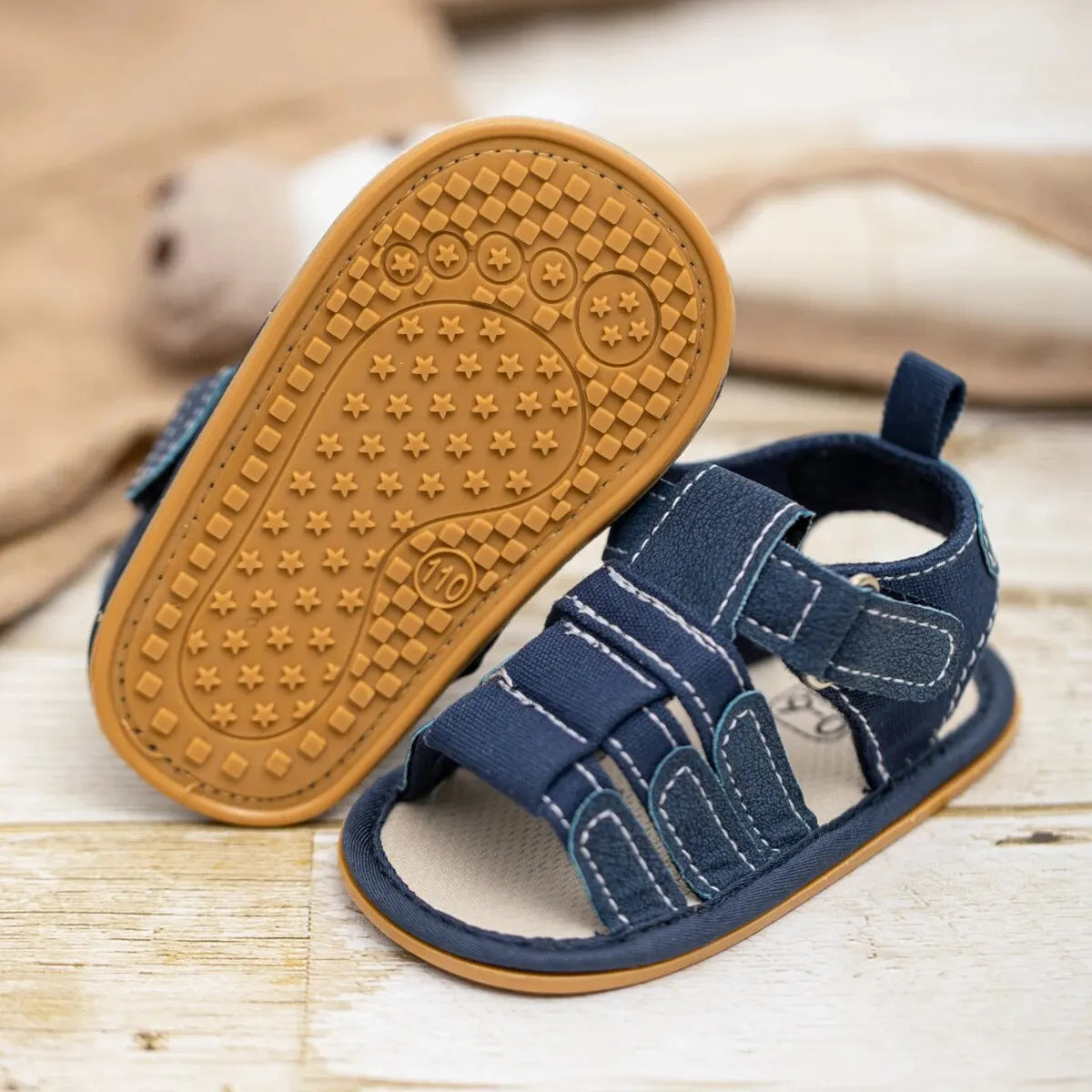 A pair of navy blue baby summer sandals with a non-slip rubber sole resting on a light wooden surface.