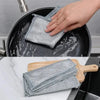 A hand is placing a stack of gray scratch-free microfiber cleaning cloths into a black frying pan.