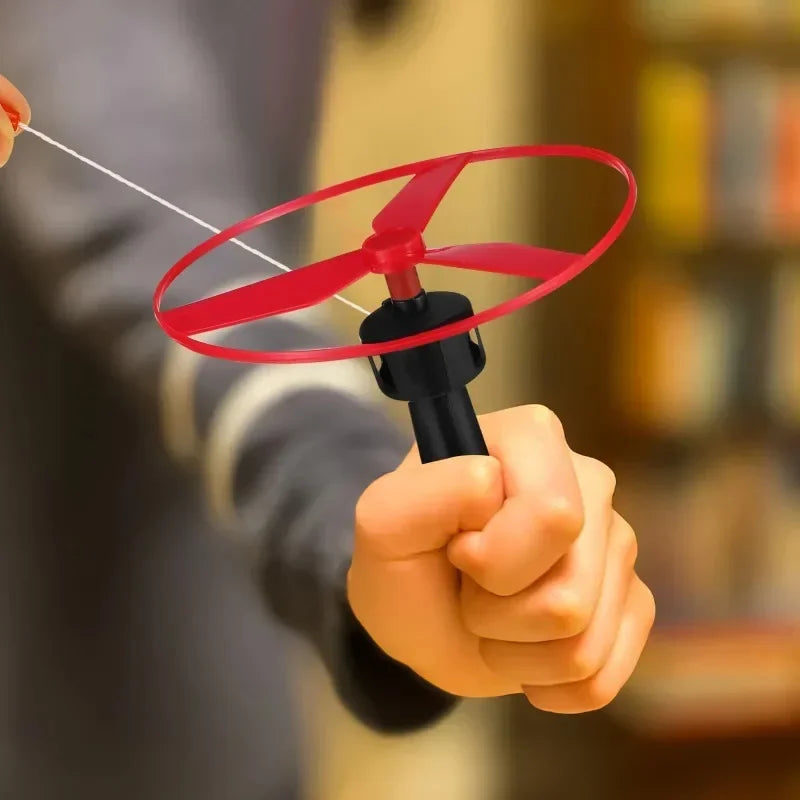 En hånd holder et rødt flyvepropel-legetøj med snor, der viser dets funktion.