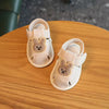 Pair of light beige soft-sole sandals for a baby featuring a cute bear design