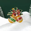 Broche navideño de campana con esmalte y pedrería, acentos rojos y verdes sobre nieve blanca.