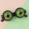 A pair of novelty funny glasses with green frames and yellow accents are shown against a light pink and green background.