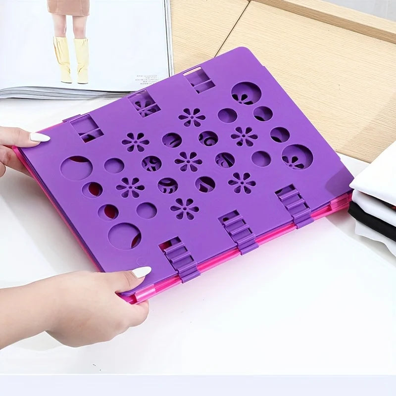 A purple clothes folding board with multiple circular and flower-shaped holes is being held by a hand on a white surface.