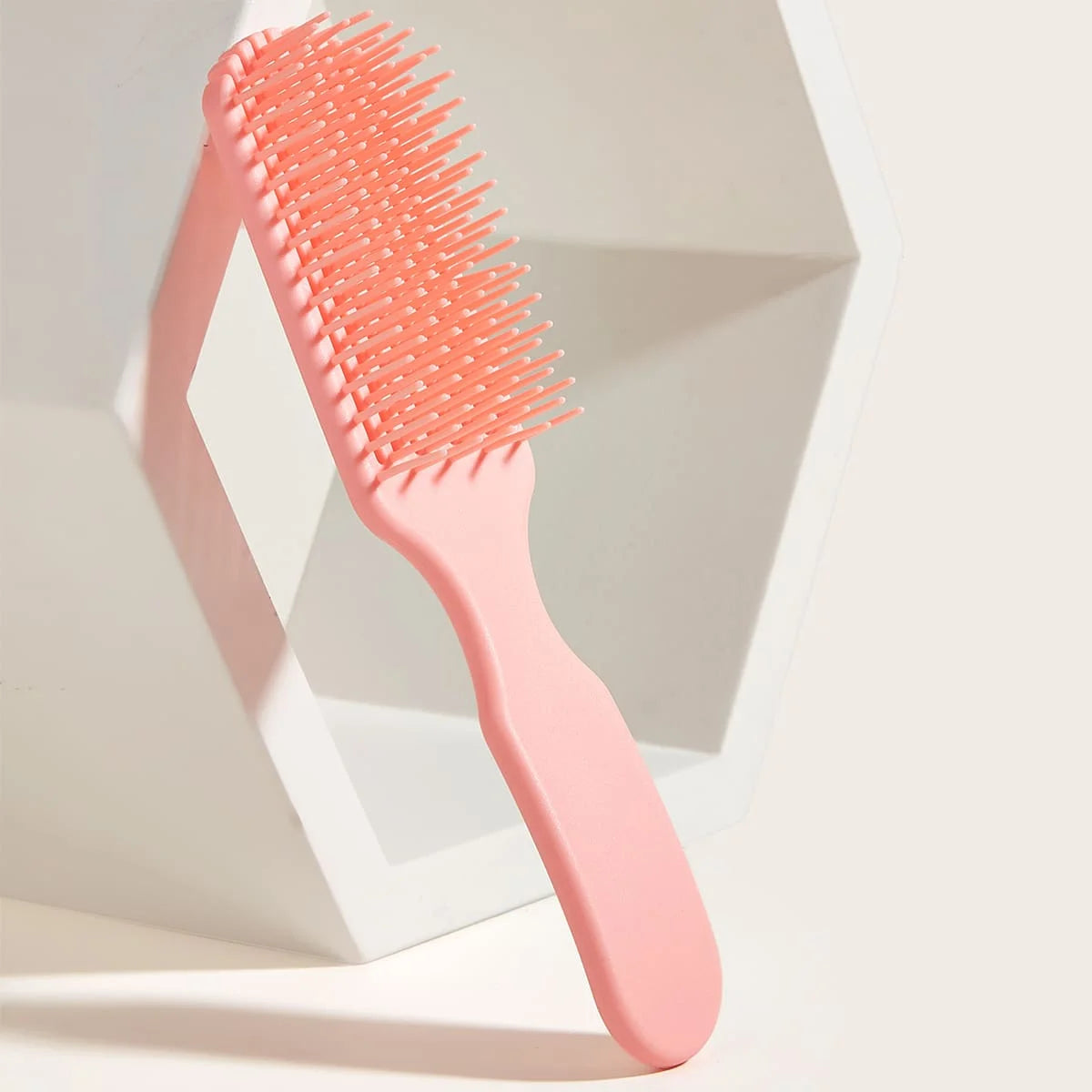 Peine desenredante rosa de 9 púas para masaje capilar dentro de un envase hexagonal blanco.