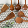 A set of natural teak wood cooking utensils, including spatulas and spoons, arranged on a gray checkered cloth.