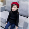 A young girl wearing a black knit turtleneck sweater and dark blue jeans, sitting on a gray sofa.