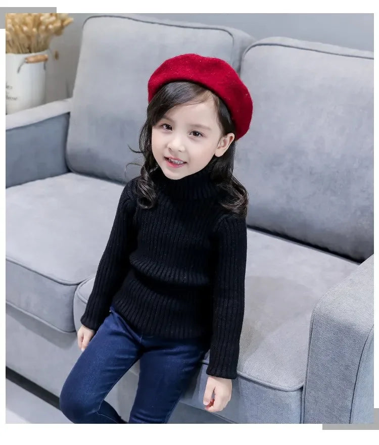 A young girl wearing a black knit turtleneck sweater and dark blue jeans, sitting on a gray sofa.