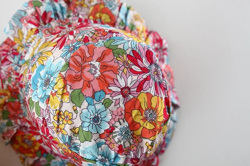 A close-up of a baby girl's floral print dress and matching hat with colorful flowers.