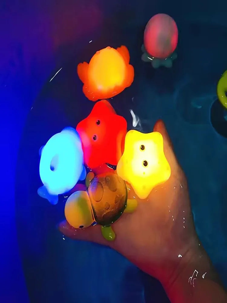 A hand is dipping colorful LED light-up animal bath toys into water, showing various glowing shapes.
