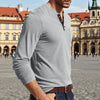 A man wearing a gray long-sleeve shirt with a collar and chest pocket, standing in front of historic European architecture.