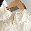 A cream-colored dress with white lace trim and small floral embroidery is displayed on a wooden hanger.