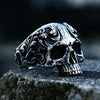 A silver gothic carved skull ring in 316L stainless steel resting on a dark surface.