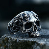 A silver gothic carved skull ring resting on a dark, textured surface.