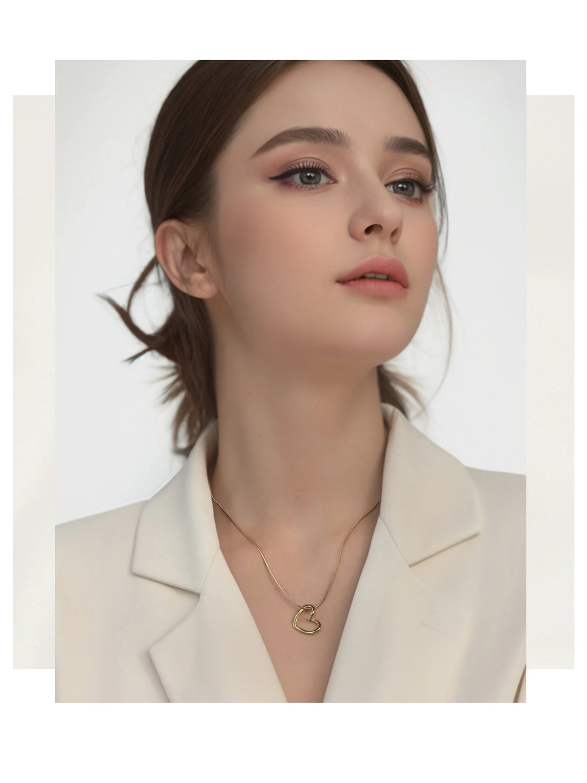 A close-up of a woman wearing a dainty gold heart pendant necklace with a snake chain.