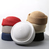 A stack of straw pillbox sun hats in various natural and solid colors, including red, beige, gray, and navy.