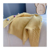 A yellow knitted cardigan sweater with a pom-pom trim is displayed on a white surface.