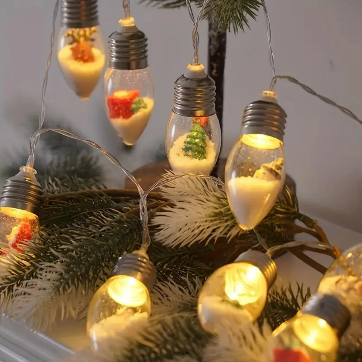 String-lys med glasspærer formet som snøballer og festlige julepynt hengende på en furugren