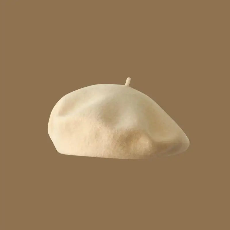 A light beige wool beret hat resting on a plain brown background.