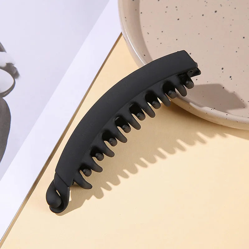 Clip de banana acrílico negro mate para el cabello sobre una superficie amarilla clara.