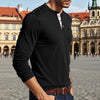 A man wearing a black long-sleeve shirt with a chest pocket and dark jeans standing in a historic European square.